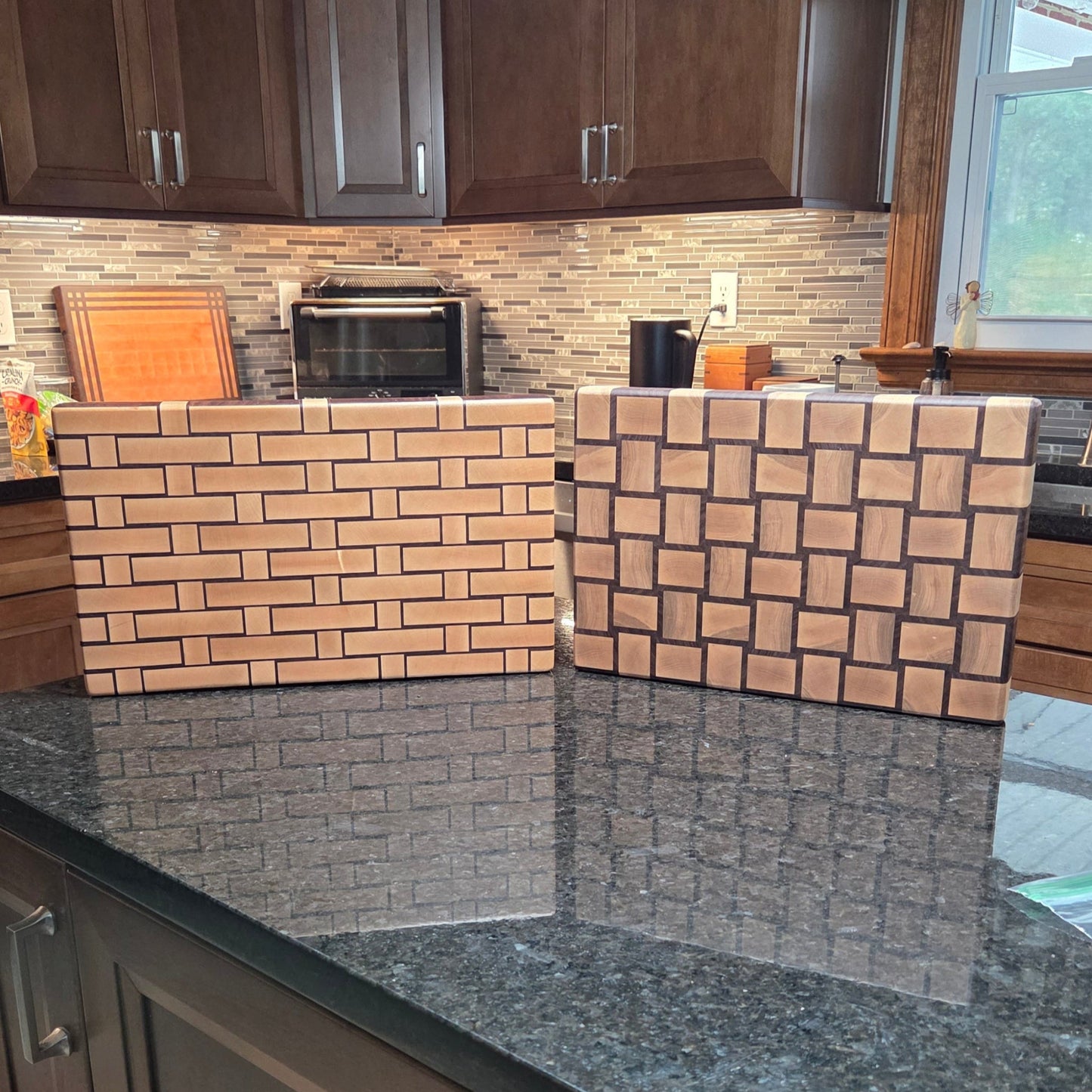 Wooden Cutting board with a woven pattern to look like it's made from wicker sitting next to a classic square basket weave style cutting board.