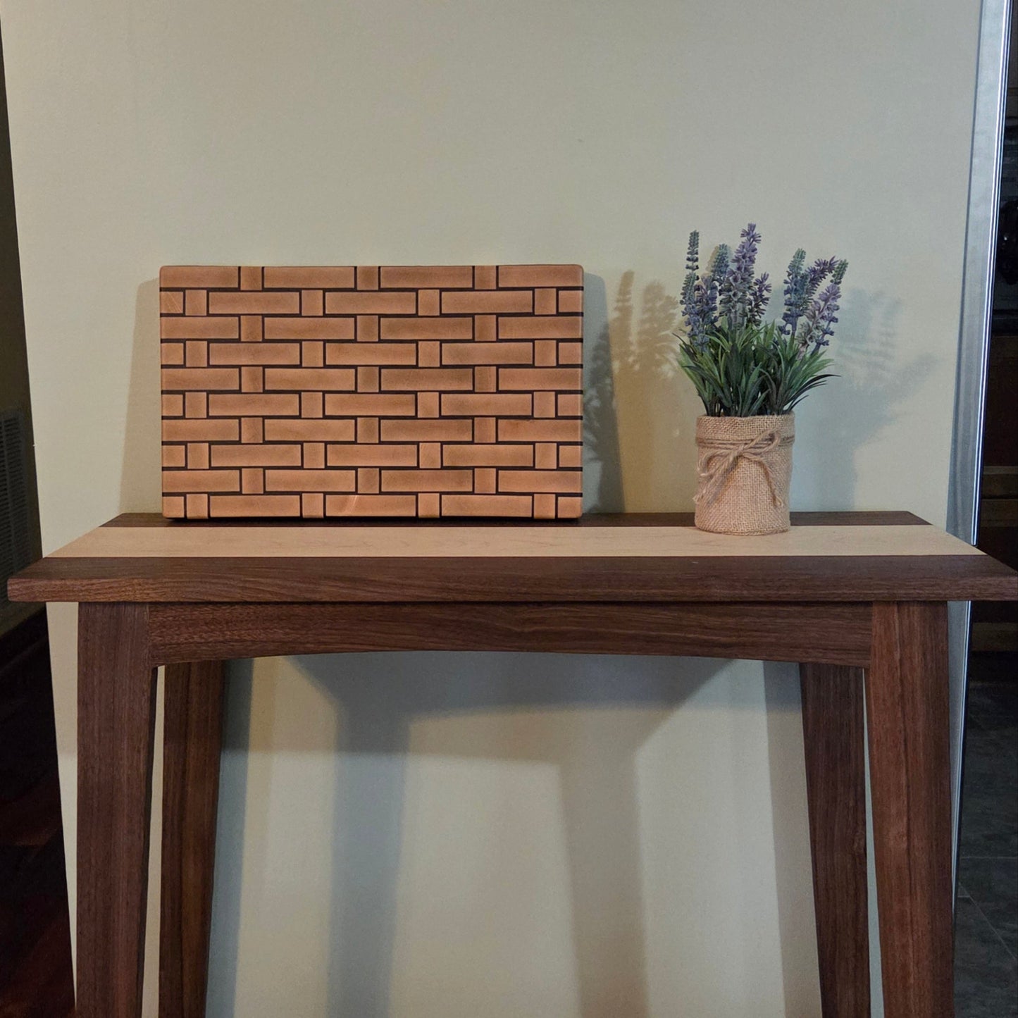 Wooden Cutting board with a woven pattern to look like it's made from wicker. Sitting on top of a walnut console table.