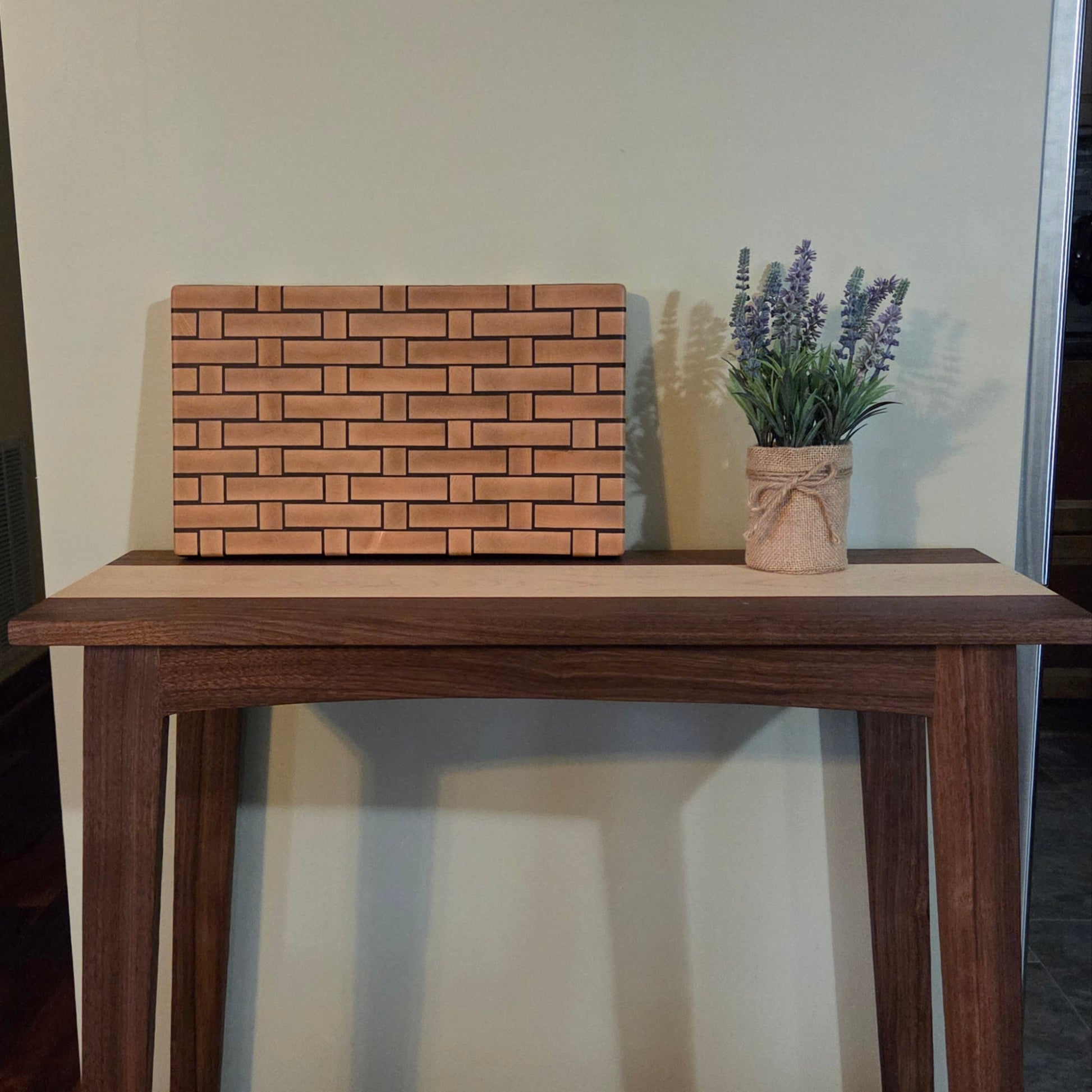 Wooden Cutting board with a woven pattern to look like it's made from wicker. Sitting on top of a walnut console table.